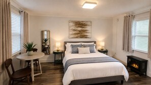 Une chambre à coucher comprenant un lit, des tables de chevet, une petite table avec des chaises, un miroir et une cheminée.