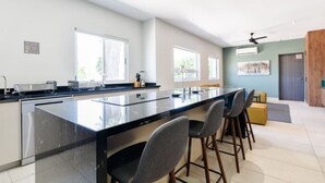 A modern kitchen with a central island, bar stools, and a dining area with a high table and chairs. - 1G Casa Curie Coliving - Cama Matrimonial + Wifi (Monterrey)