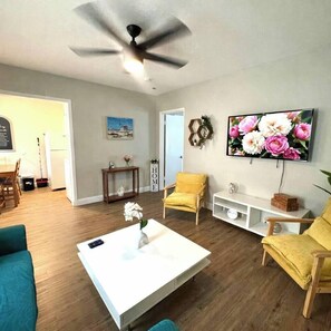 Ein Wohnzimmer mit Deckenventilator, einem an der Wand befestigten Fernseher, einem Couchtisch mit einer Vase und einem gelben Sessel.