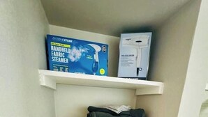 Un corridoio stretto con scaffali bianchi che ospitano un vaporizzatore per tessuti fatti a mano, un'asciugatrice di medie dimensioni, vestiti piegati e un piccolo contenitore.