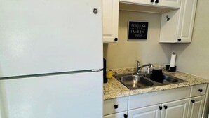 Una cucina con mobili bianchi, un lavello in acciaio inossidabile e un frigorifero.