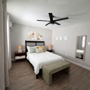 A bedroom with a bed, bedside tables, a ceiling fan, a mirror, and a wall decoration. - Coastal Charm; quick drive to the Ocean • Pets OK (Clearwater)