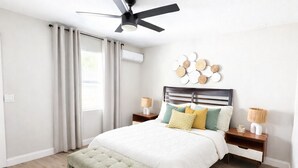 Una camera da letto con un letto, una panca, una ventola a soffitto, una lampada a parete e un elemento decorativo a parete.