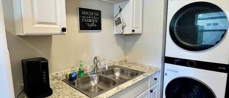 Cocina con armarios blancos, un lavamanos doble, una cafetera y una lavadora de carga frontal.