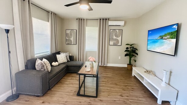 A living room with a sectional sofa, a coffee table, a ceiling fan, an air conditioning unit, a potted plant, and a framed picture on the wall. - Beach Retreat: Modern 1-Bedroom • Pet Friendly (Clearwater)