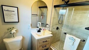 A modern bathroom with a toilet, vanity, and glass shower enclosure. - Beach Retreat: Modern 1-Bedroom • Pet Friendly (Clearwater)