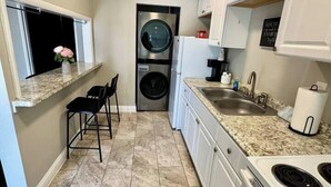 A compact kitchen with a built-in washer and dryer, a sink, a stove, and a small dining area with chairs. - Beach Retreat: Modern 1-Bedroom • Pet Friendly (Clearwater)