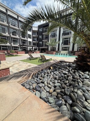 A modern building with multiple balconies, a swimming pool, and a landscaped area with rocks and palm trees. - Romantic Luxe Stay, Houston, Texas. (Houston)
