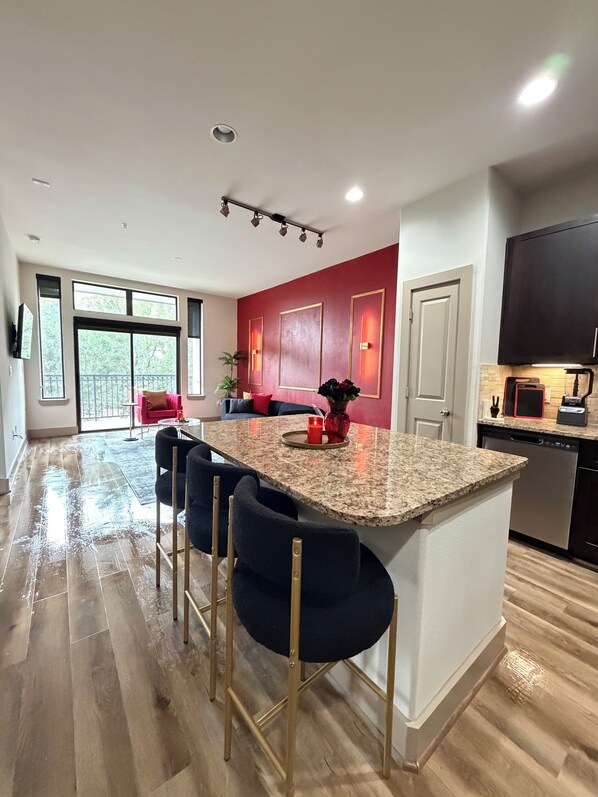 A modern kitchen with a granite countertop, bar stools, and a red accent wall. - Romantic Luxe Stay, Houston, Texas. (Houston)