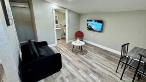 Ein Wohnzimmer mit einem schwarzen Sofa, einem runden Tisch und einem an der Wand montierten Fernseher.