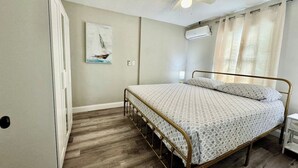 Ein Schlafzimmer mit Bett, Deckenventilator, Klimaanlage, einem Bild und einer Tür.