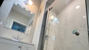 Een moderne badkamer met een douchecabine van glas, een wit badkamermeubel met lades en een grote spiegel boven de wastafel.