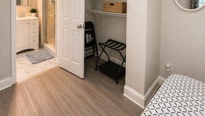 Een slaapkamer met een bed, een kledingkast met planken, een spiegel en een deur naar een badkamer.