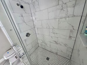 Ducha con puerta de cristal, azulejos de mármol blanco y un patrón de suelo hexagonal.