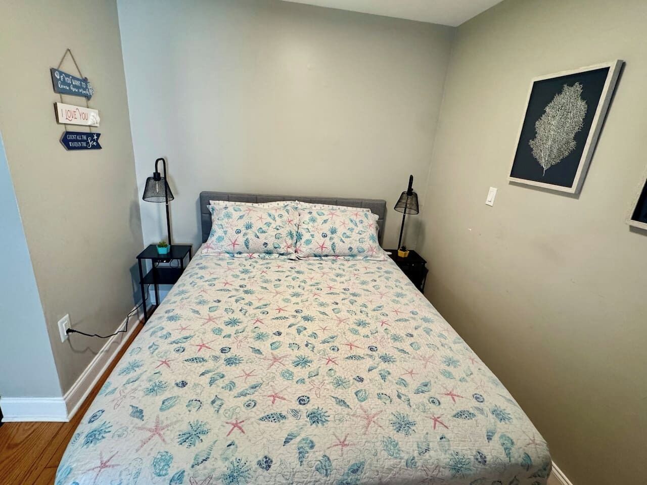 Une chambre à coucher comprenant un lit, des tables de chevet, une lampe fixée au mur et une œuvre d’art encadrée.