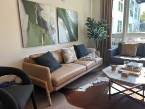 A modern living room with a leather sofa, a coffee table with books and glasses, a large plant, and abstract wall art. - Luxury & Cozy 1-bedroom apartment with AC in tranquil Sacramento next to Capitol (Sacramento)