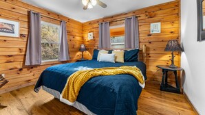Ein Schlafzimmer mit einem Bett, Holzwänden, einem Deckenventilator und einem Fenster mit Vorhängen.