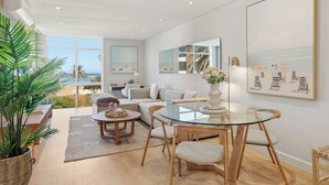 A modern living room with a glass table, sofas, a large potted plant, and artwork on the walls. - 2 Bed Beachfront Home with Panoramic Sea Views - Steps from the Beach (Cape Town)