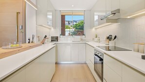 A modern kitchen with white cabinetry, a wooden countertop, a built-in oven, and a view of a hillside. - 2 Bed Beachfront Home with Panoramic Sea Views - Steps from the Beach (Cape Town)