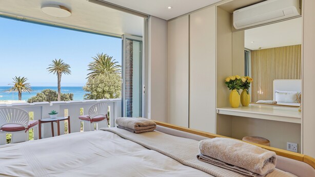 A bedroom with a bed, a small table, two chairs, a mirror, and an air conditioning unit. - 2 Bed Beachfront Home with Panoramic Sea Views - Steps from the Beach (Cape Town)