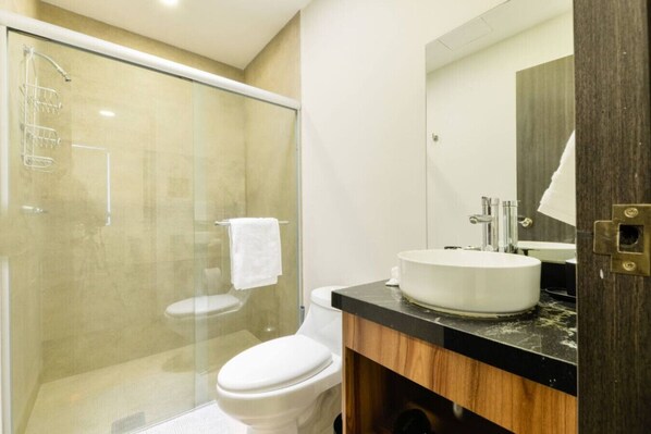 A modern bathroom with a glass-enclosed shower, a white toilet, and a sink with a large mirror. - 1F Casa Curie Coliving - Cama Matrimonial + Wifi (Monterrey)