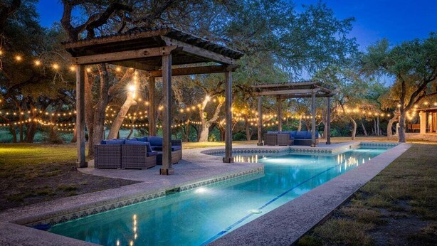 Une piscine agrémentée d’une pergola et de guirlandes lumineuses, entourée d’arbres.