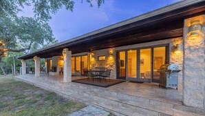 Une maison moderne dotée d’un patio couvert, de piliers en pierre et d’un espace barbecue.