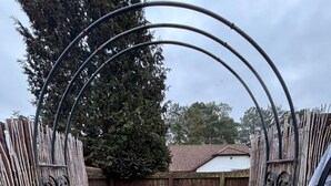 Un área exterior cercada con suelo de grava, una reja metálica y una valla de madera.