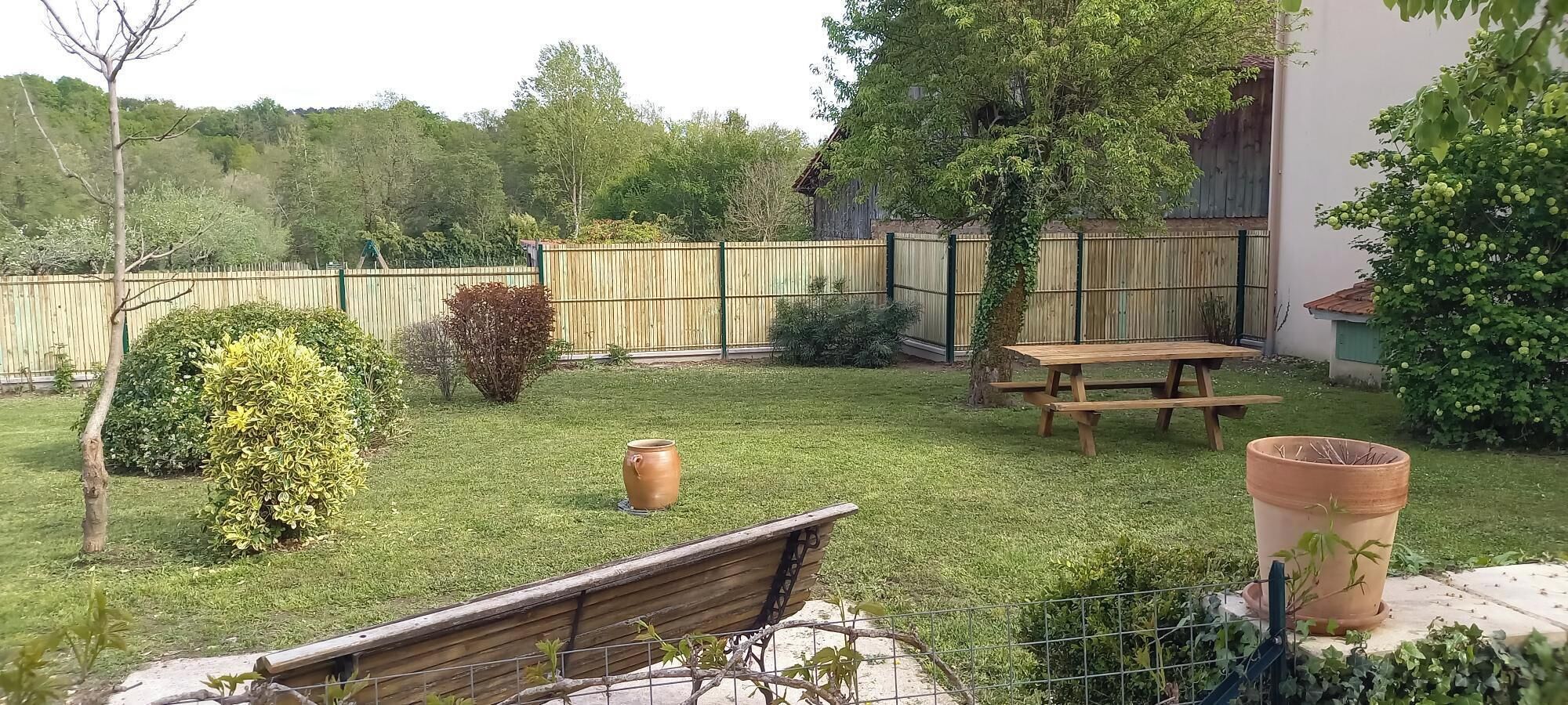 Un jardin avec une clôture en bois, un banc en bois et un grand pot en terre cuite.