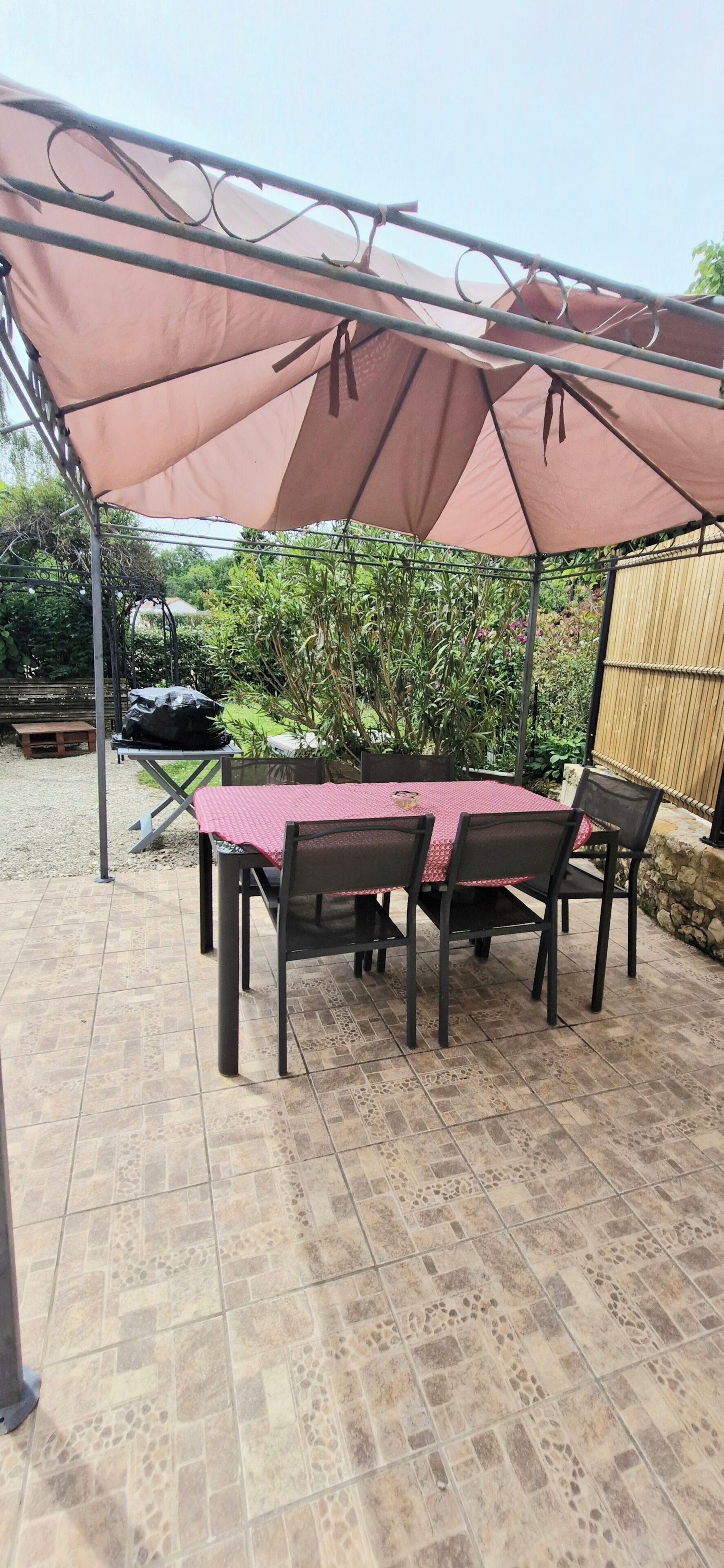 A covered patio area with a table and chairs, surrounded by a metal fence and a bamboo fence.