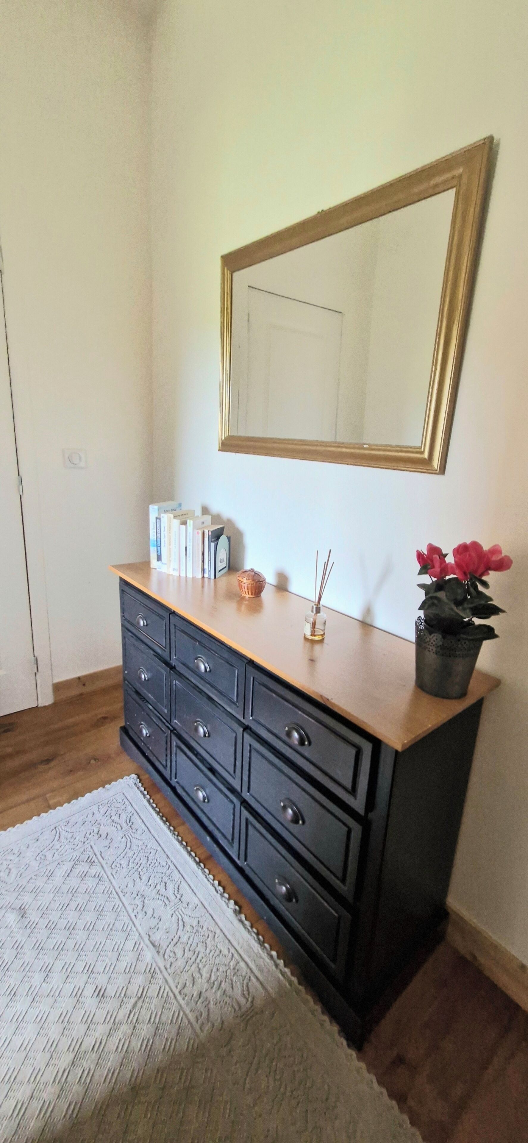 A room with a wooden dresser, a mirror, a potted plant, and a patterned rug.