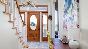 A staircase with wooden balusters, a chandelier, a wooden door with an oval glass panel, and a colorful abstract painting on the wall. - Unique Victorian Home*Pool*Pets*Firepit (Dripping Springs)