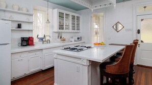 Una cocina con armarios blancos, una isla central y un comedor con sillas de mimbre.