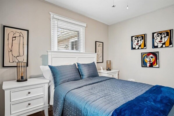 Une chambre à coucher avec un lit, une table de chevet, une commode et des œuvres d’art accrochées aux murs.
