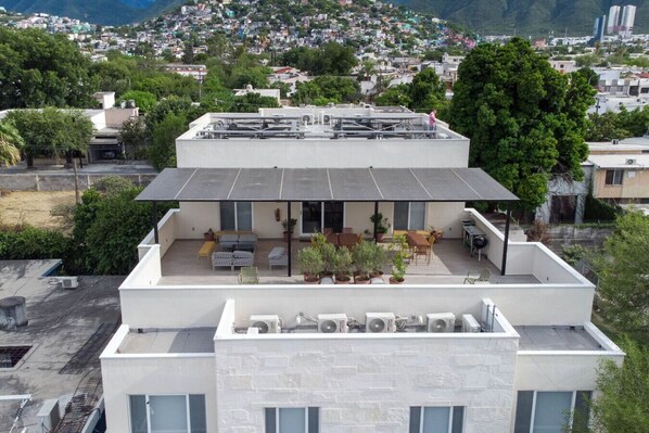 Un bâtiment moderne doté d’une terrasse sur le toit, aménagée avec du mobilier d’extérieur et des plantes en pot.