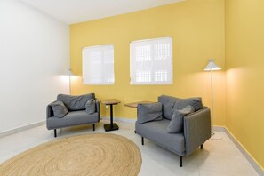 Une pièce avec deux canapés gris, un petit tapis rond, deux petites tables et deux lampadaires.