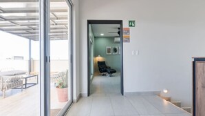 Un couloir d’hôtel avec une porte en verre donnant sur un balcon, une chaise et une lampe en arrière-plan.