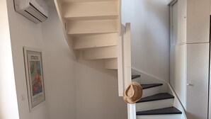 A staircase with a hat on the railing, a framed picture on the wall, and a white air conditioning unit. - Duplex with panoramic terrace - Centre, Saint-Paul-de-Vence - Air conditioning & WiFi (Saint-Paul-de-Vence)