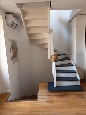 Eine Treppe mit Hut auf der Geländer und ein gerahmtes Bild an der Wand, sowie eine weiße Klimaanlage.