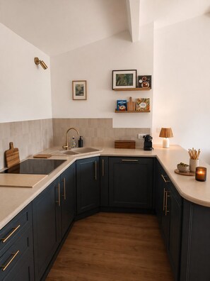 Une cuisine moderne avec des meubles de couleur sombre, un grand îlot central et un plan de travail sur lequel sont disposés divers objets.