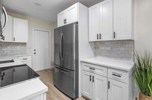 Una cocina moderna con armarios blancos, un refrigerador de acero inoxidable y una estufa negra.