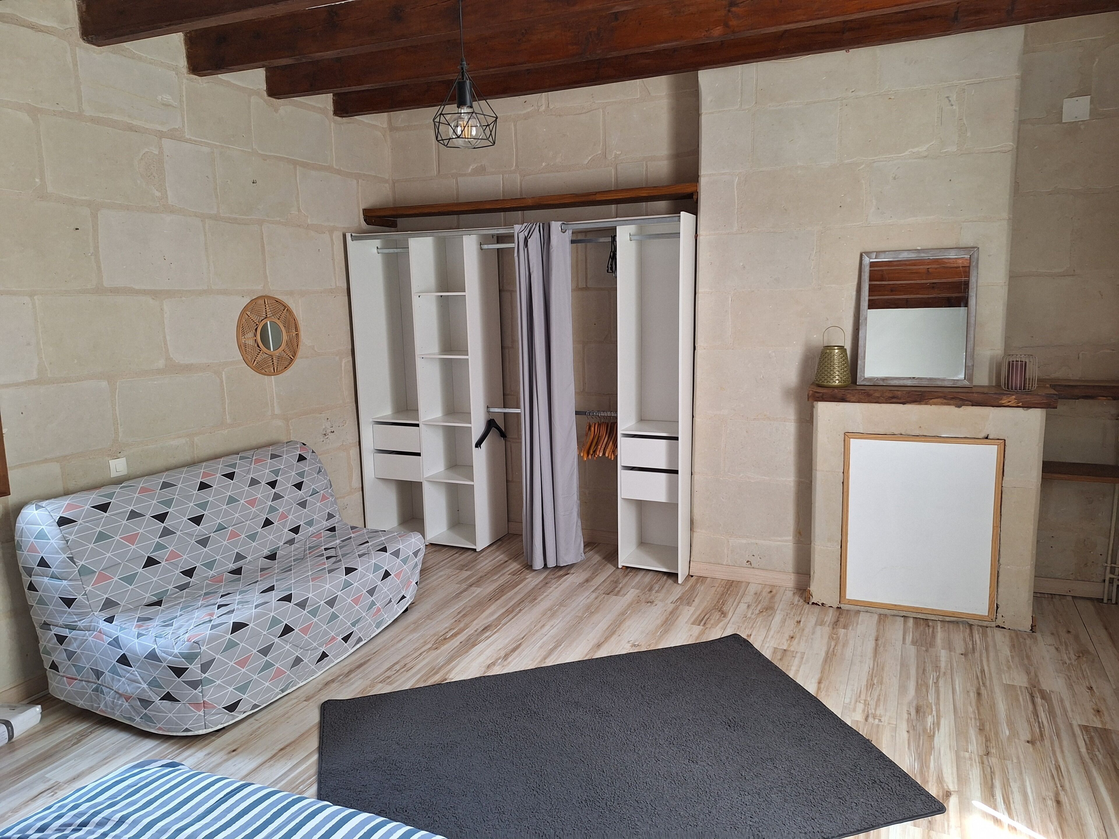 A room with a patterned sofa, a grey rug, a wardrobe, a mirror, and a small cabinet.