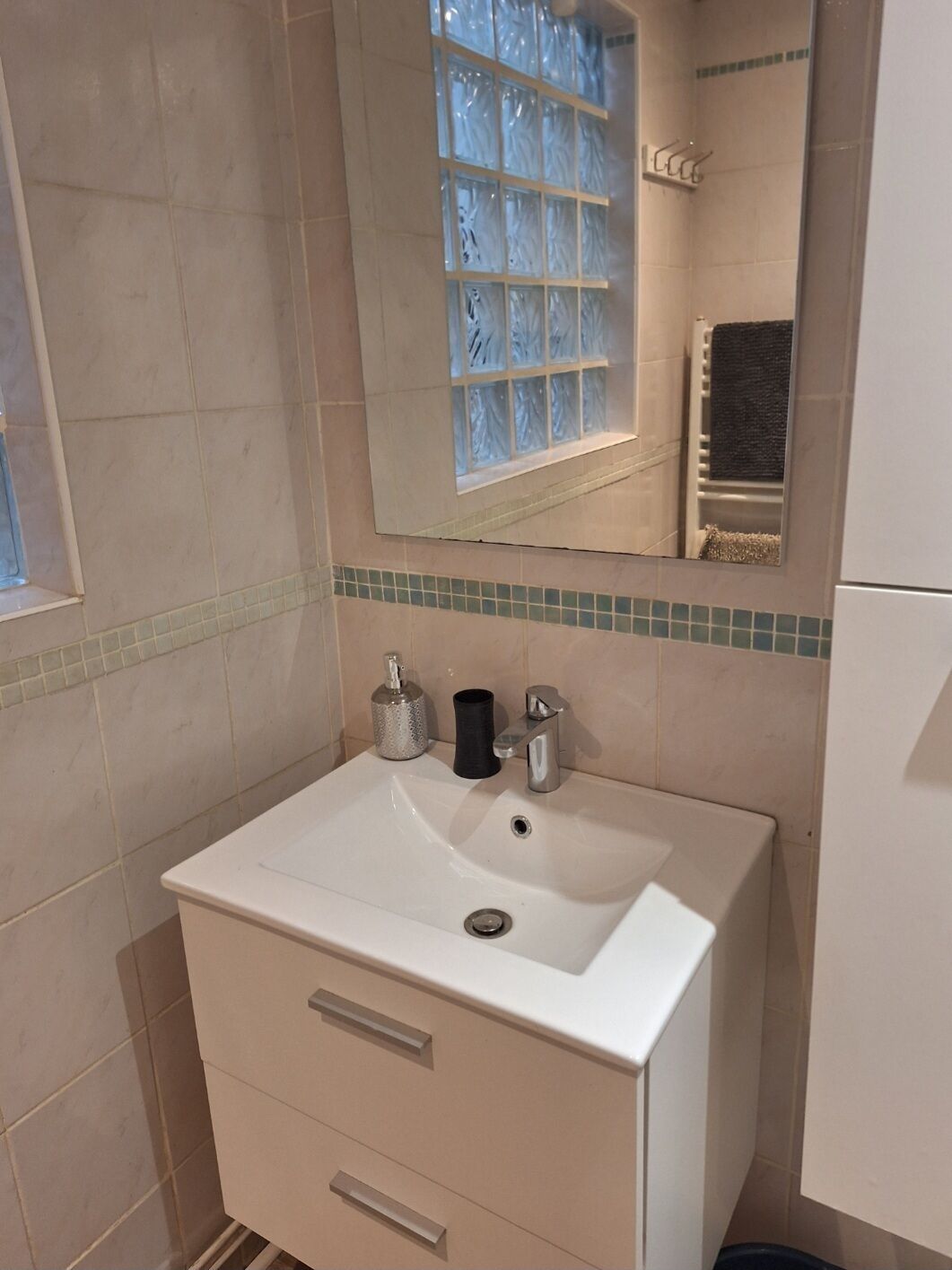 A bathroom with a white sink, a mirror, a window with frosted glass, and a towel rack.