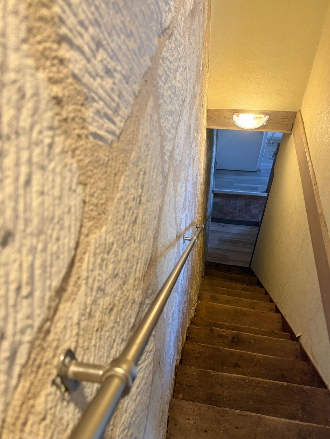 Un escalier en bois, doté d’une rampe, mène à un palier où se trouve un luminaire.