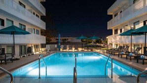 Ein Schwimmbecken mit Liegestühlen und Sonnenschirmen, umgeben von mehrstöckigen Gebäuden.