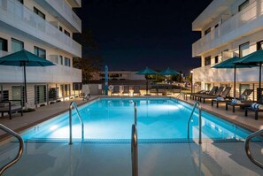 Una piscina con sillones de descanso y sombrillas, rodeada de edificios de varios pisos.