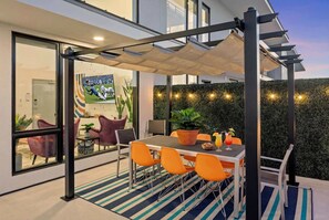 Un patio al aire libre con una mesa, sillas, una pérgola y un muro de setos.
