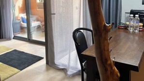 Ruokailutilassa on puinen pöytä, tuolit, suuri puunrungosta veistetty koriste-esine sekä lasiovesta avautuva näkymä ulkotilaan.
