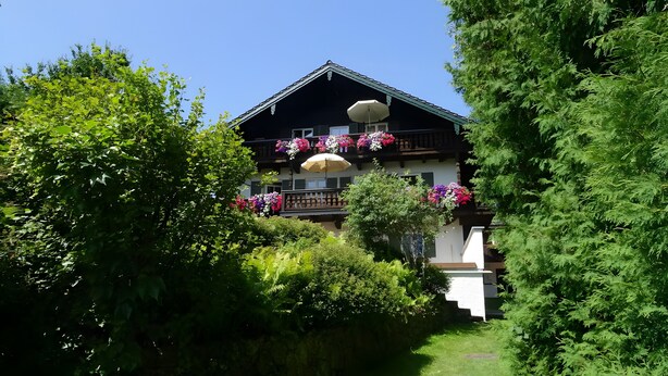 Un edificio de dos pisos con balcones decorados con flores, rodeado de abundante follaje.