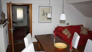 A room with a dining table, red sofa, and a framed artwork on the wall.